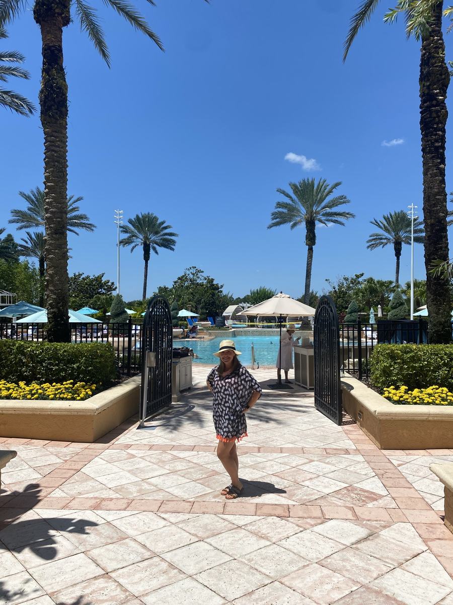 Amber standing near a resort pool lined with palm trees