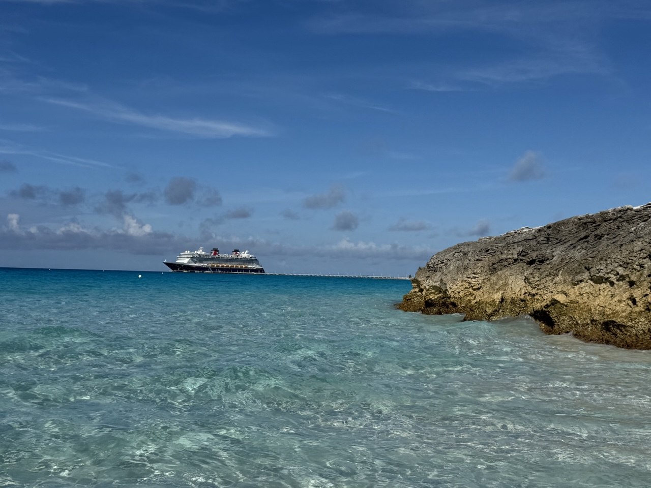 Turquoise water with a cruise ship in the distance near rocky shoreline